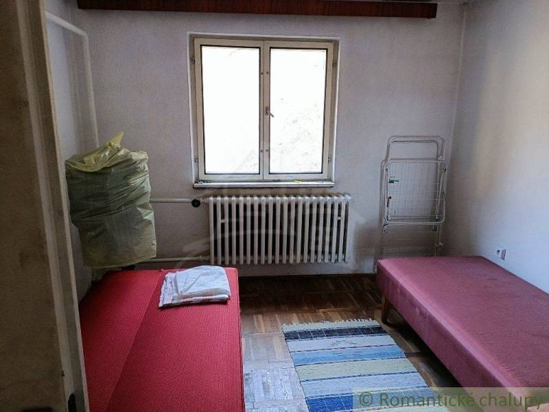 A room with two beds and a small carpet. Through the window, there is a view of nature.