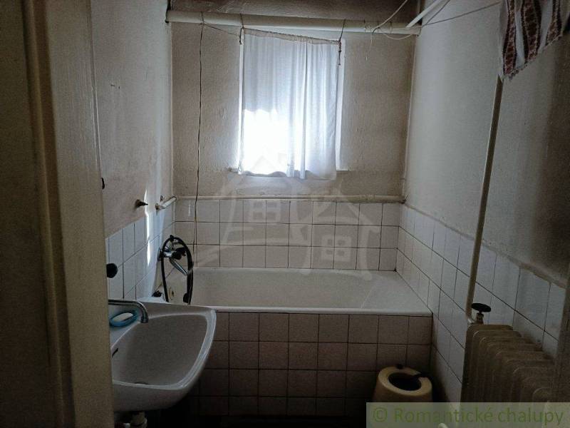 An older bathroom with a bathtub and a sink in a cabin, light through a small window.