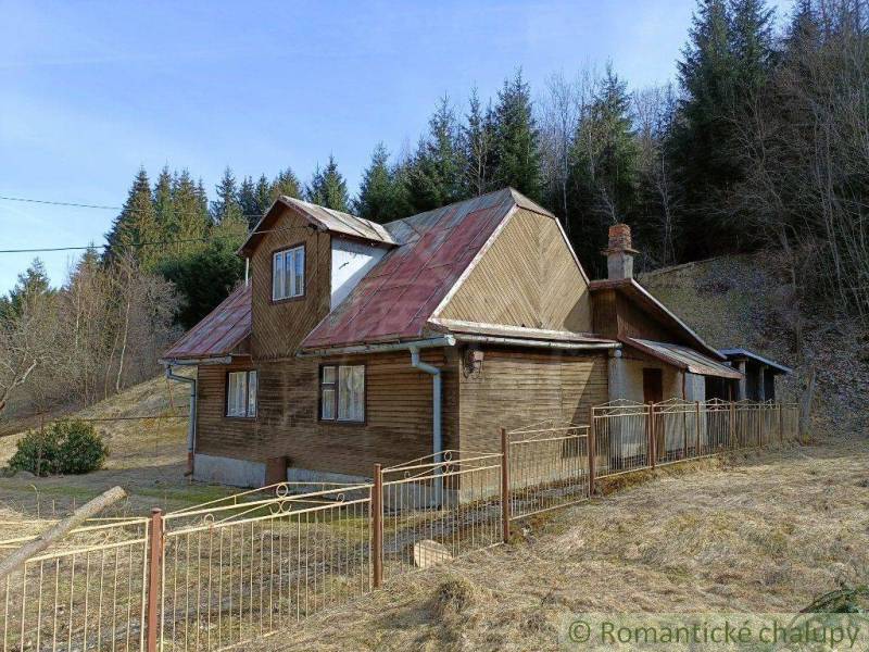 A cottage in Veľké Rovné with a wooden exterior and a metal fence in a forest environment.