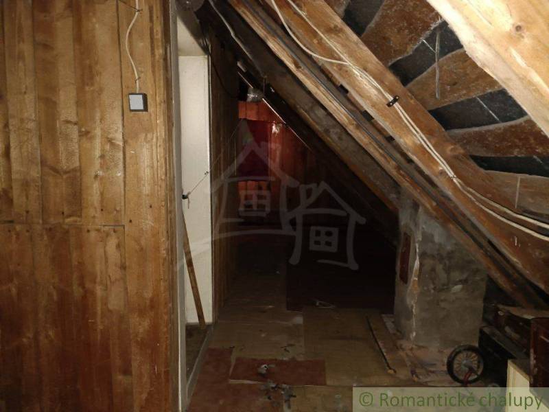 A dark attic hallway in a cabin with slanted wooden walls and electrical wires.