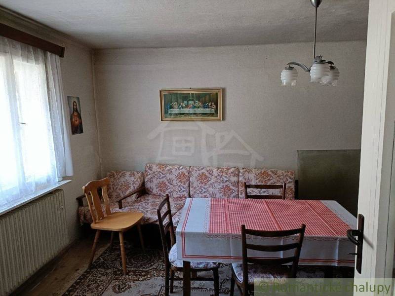 A room with wooden chairs, a table, and a red tablecloth, ideal for a cottage.