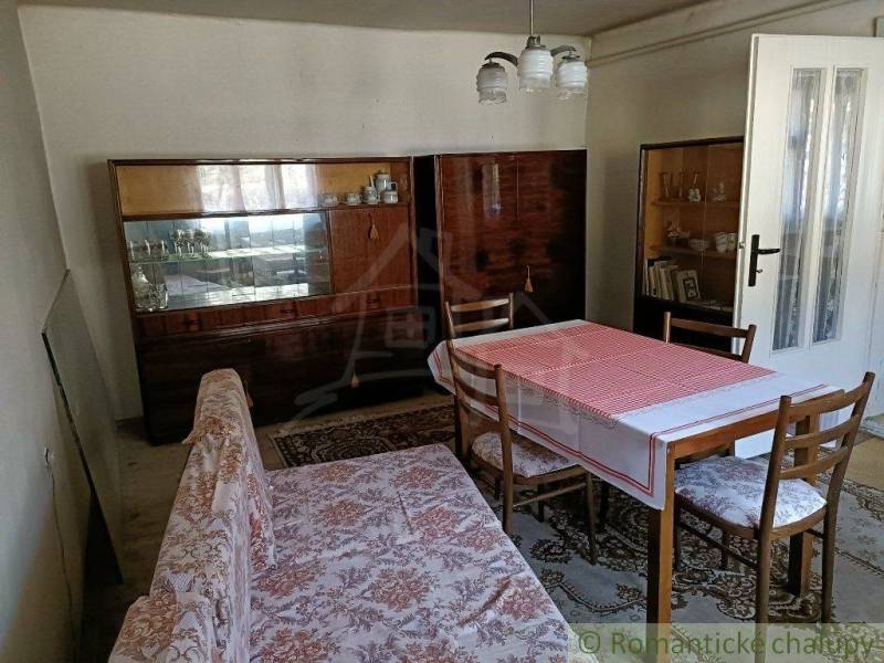 A dining table with a tablecloth and chairs in a simple cabin with wooden furniture.