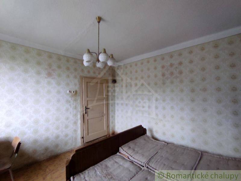 A room in a family house with a bed, vintage wallpaper, and a retro chandelier.