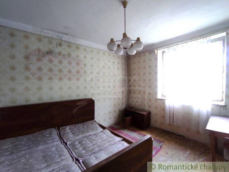 Bedroom in a family house with a double bed, wallpaper, and mold on the wall.
