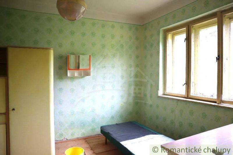 A room in a family house with a simple bed, a wardrobe, and shabby walls.