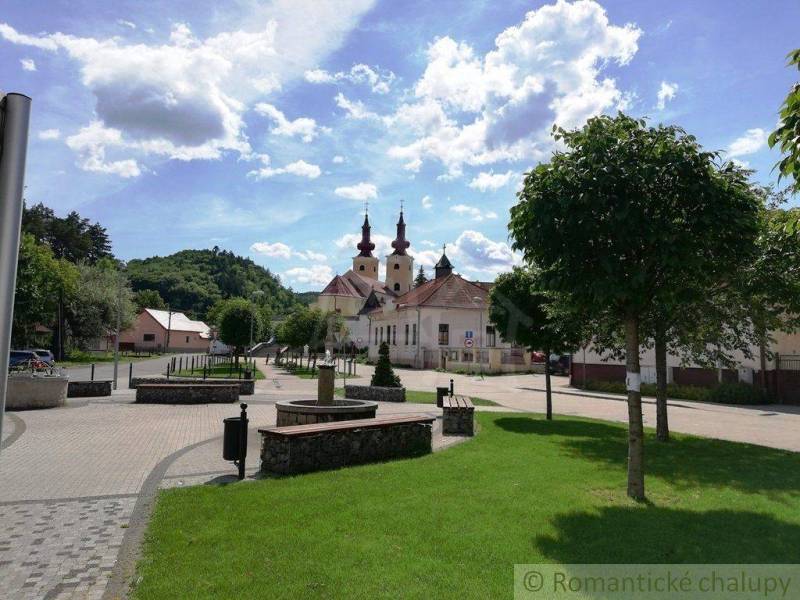 Square with a church and garden, trees, benches, hills and houses in the background.