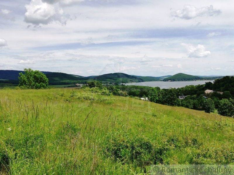 A vast meadow with a view of hills, greenery, and a water reservoir, ideal for gardens.