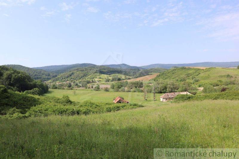 A vast meadow surrounded by hills, with a family house and a village visible in the background.