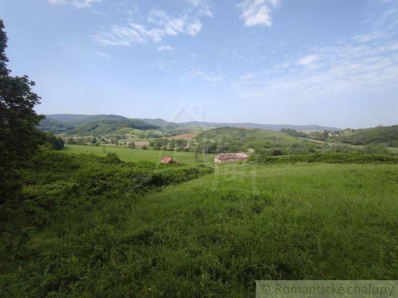 A vast meadow in the valley with a family house surrounded by hills and greenery.