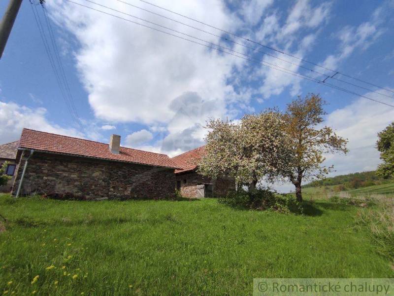 A stone house with trees on a rural property under a bright sky.