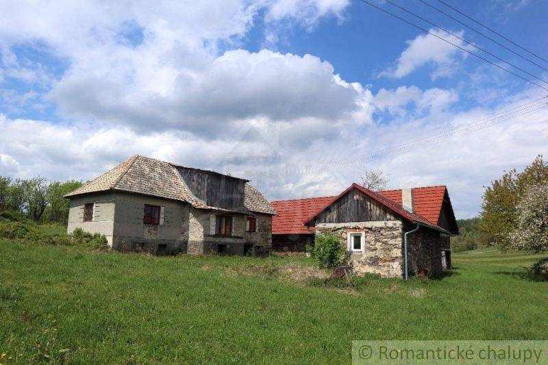 Stone family house with a red roof on a green plot under a blue sky.
