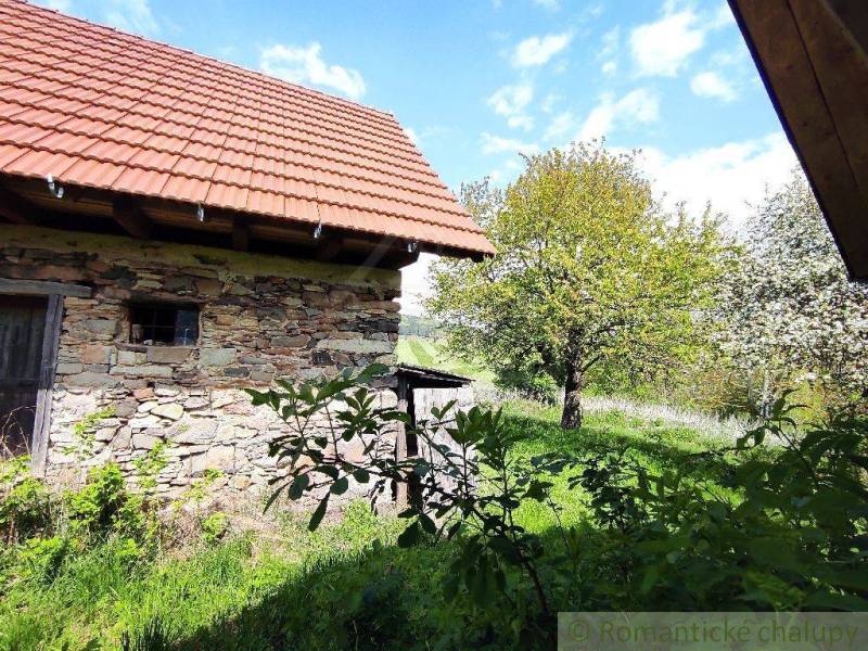 The picture shows a stone family house surrounded by greenery and trees in an idyllic landscape.