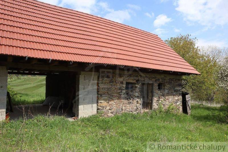 An old stone house, under a red roof, surrounded by nature, offers peaceful living.