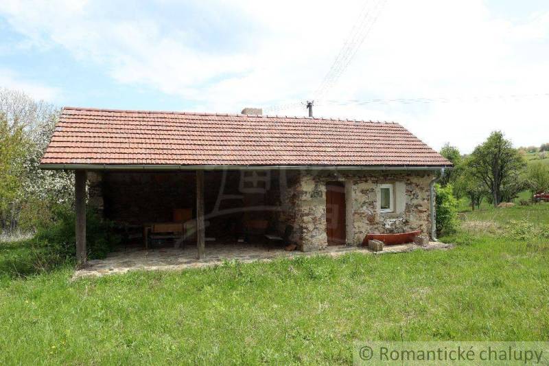 A cottage with stone walls and a tiled roof situated on a spacious green plot.