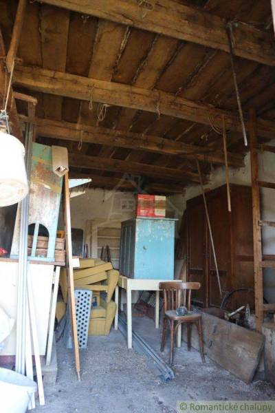 A mess in a wooden shed with old furniture, chairs, and a shelf near the family house.