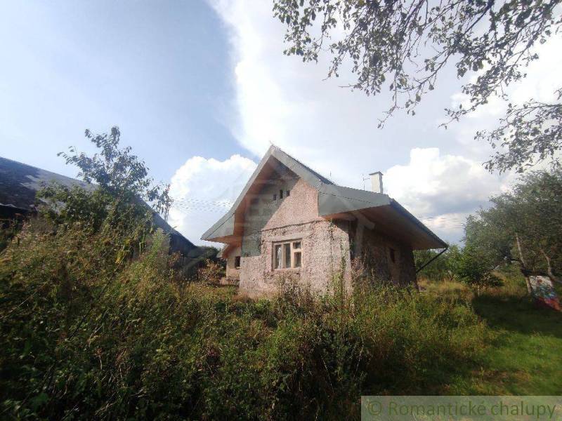 An older family house in the countryside, surrounded by greenery and trees, under a clear blue sky.