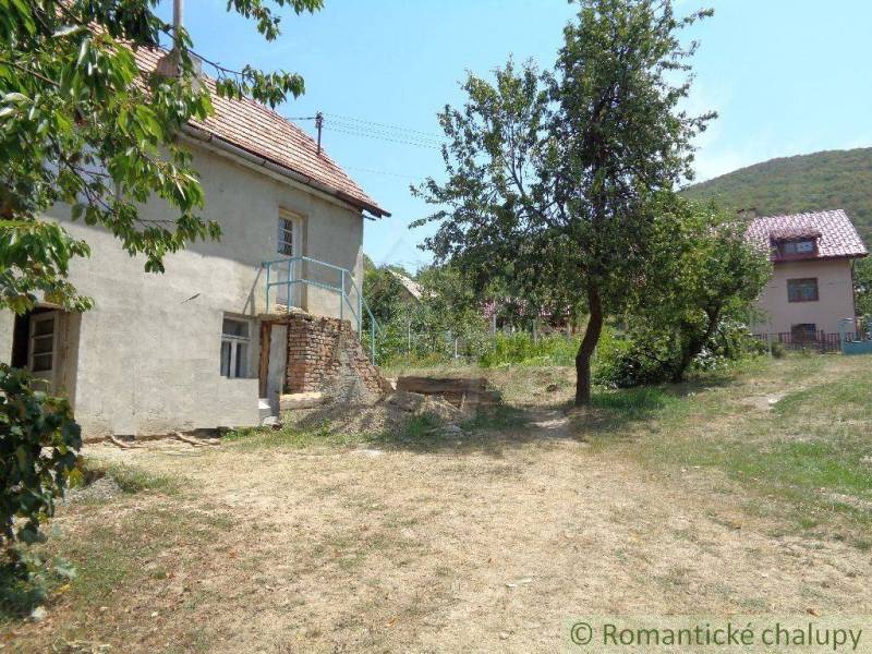A family house in the countryside with a spacious lawn, trees, and a neighboring building in the background.