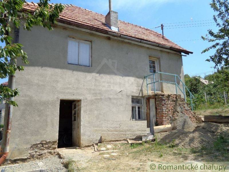 A family house with a simple facade, a garden, and trees in a peaceful rural setting.