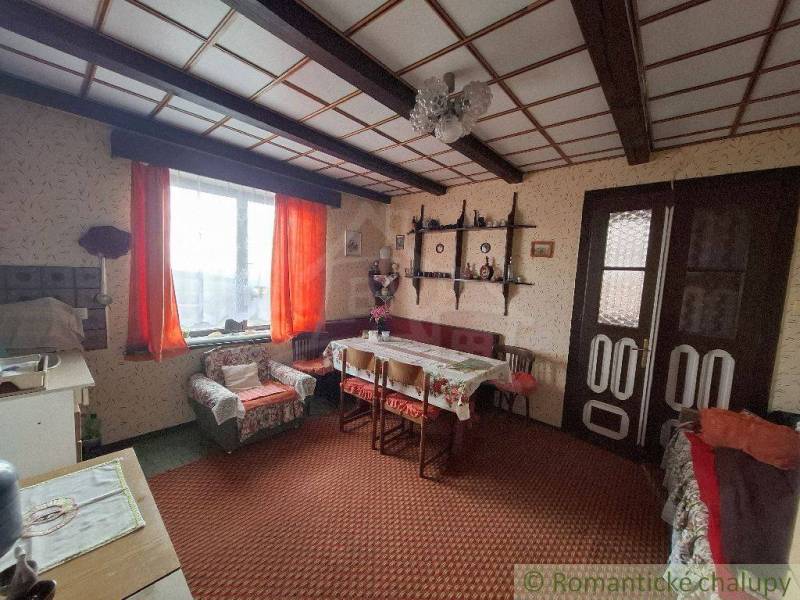 A traditional living room with rustic furniture, orange curtains, and a wooden ceiling, evoking the coziness of a cottage.