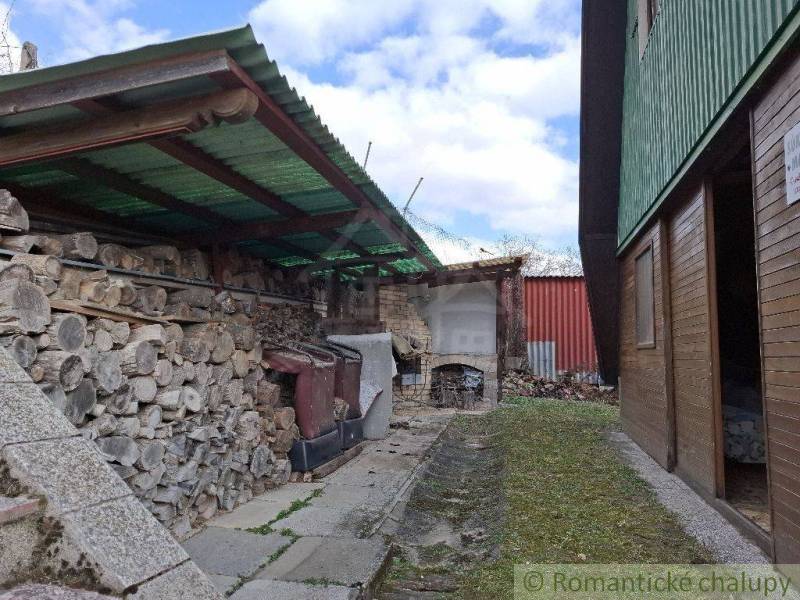 Garden cottage with wood under the shelter, fireplace in the background in the yard.