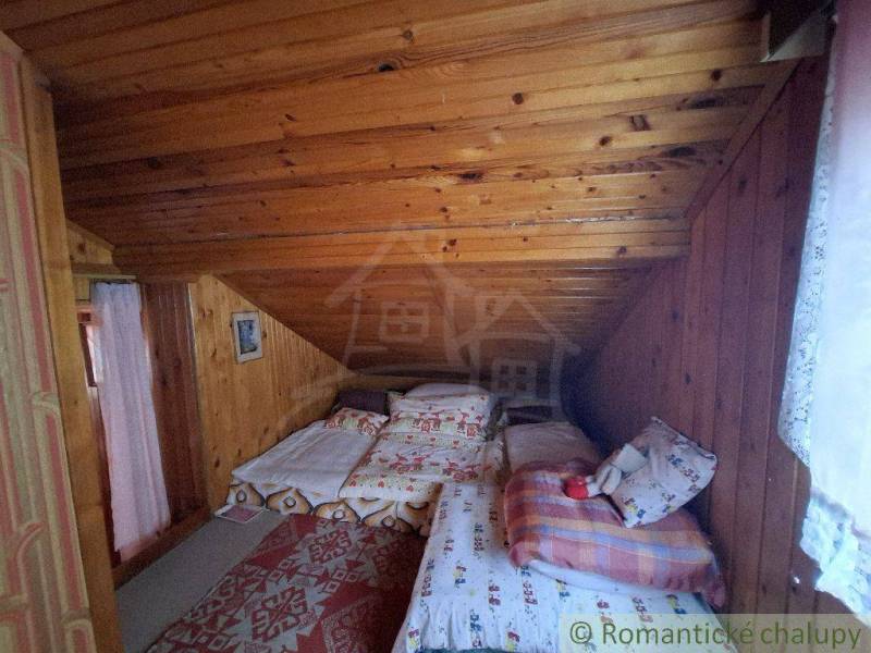 A rustic cabin with wooden walls and beds in the loft under a sloped roof.