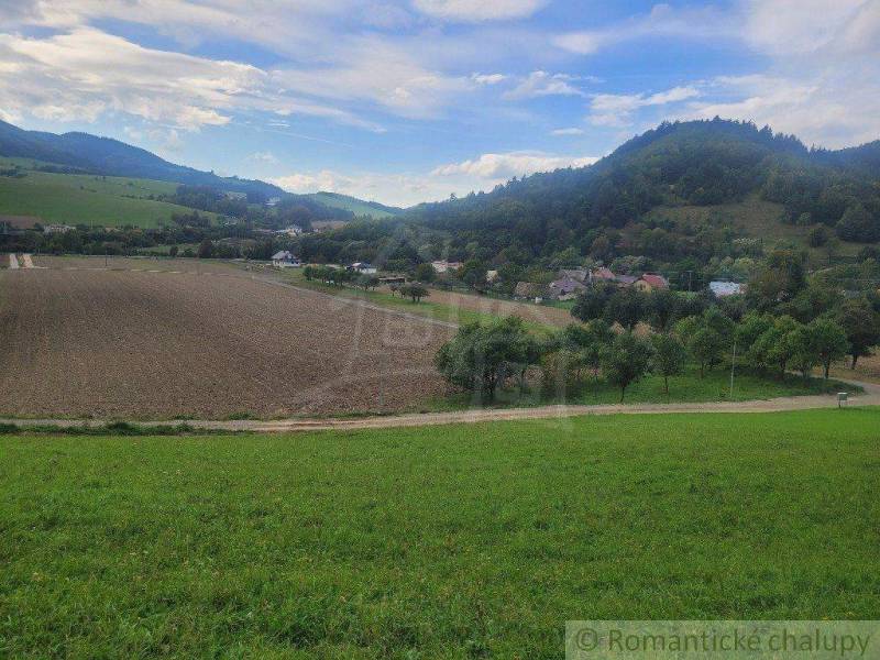 A valley with green fields, fields, trees, and hills in the background under a blue sky.