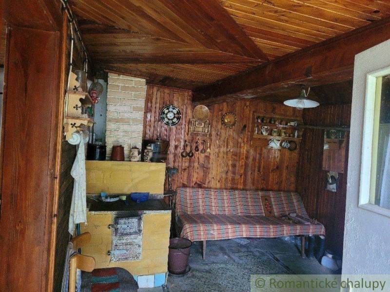 The interior of a cottage with a wooden wall, a couch, and a traditional tiled stove in a family house.