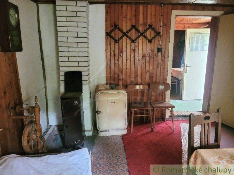 The interior of a traditional cottage with wooden walls, an old stove, and a tiled stove.