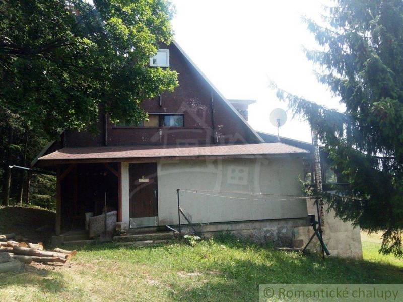 A cabin surrounded by trees in a natural setting with a wooden porch and a satellite dish.