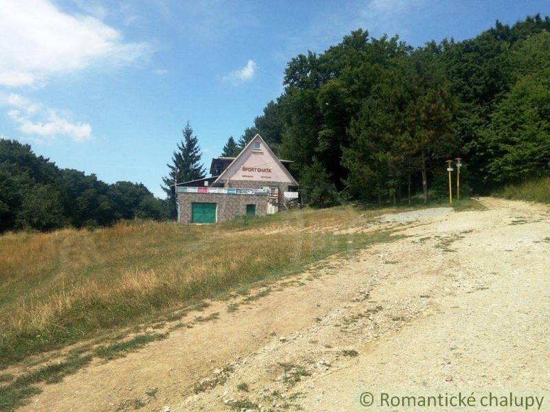 A cottage in the middle of nature surrounded by grassy slopes and forests.