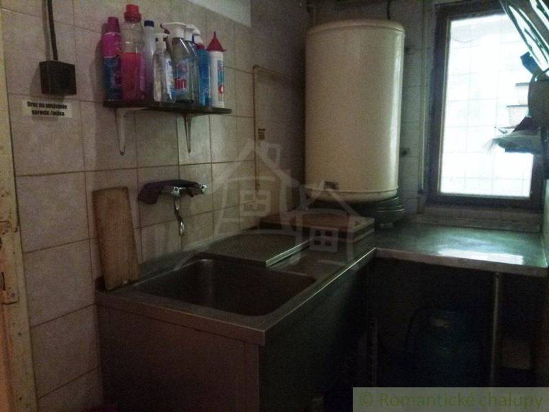 A kitchen with a sink in a cottage, cleaning products on the shelf.