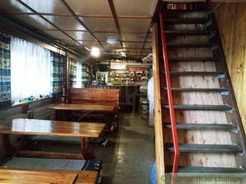 In a cozy cabin with wooden tables and a staircase, there is a bar with drinks and snacks.