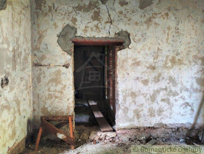 The image shows a neglected interior of a family house with old plaster and a wooden support.