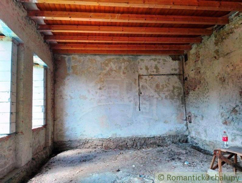 Unfinished interior of a family house, exposed wooden ceilings, old plaster, light penetrating through the windows.
