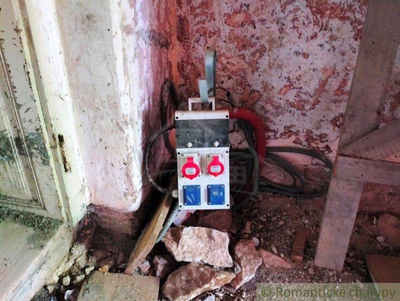 An electrical distribution box in the corner of a family house room, surrounded by stones and a wall.