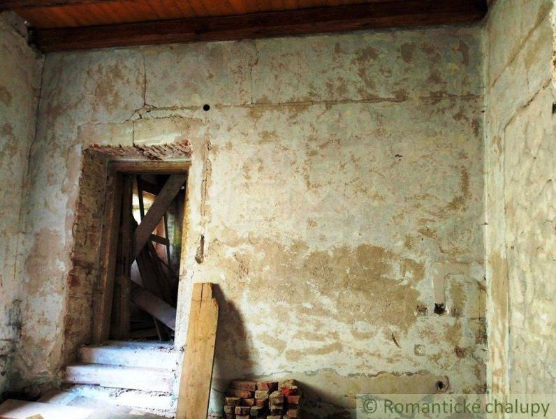 The dilapidated interior of an old family house with an exposed brick wall and wooden planks.