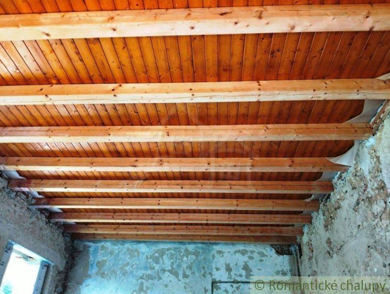 A wooden beam ceiling in a family house, with plastered walls and exposed bricks.