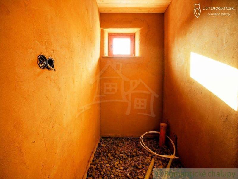 Interior with clay walls, a window, round piping, and a pebble floor, suitable for a family house.