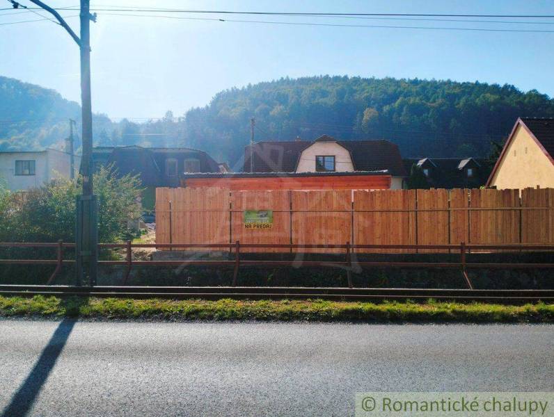 The family house is for sale, surrounded by a fence, nearby buildings, and beautiful nature.