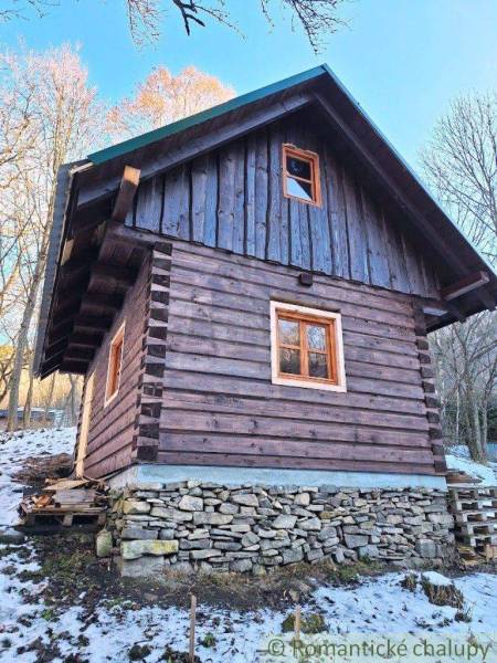 A wooden cabin stands on stone foundations in the middle of nature with the first signs of snow.