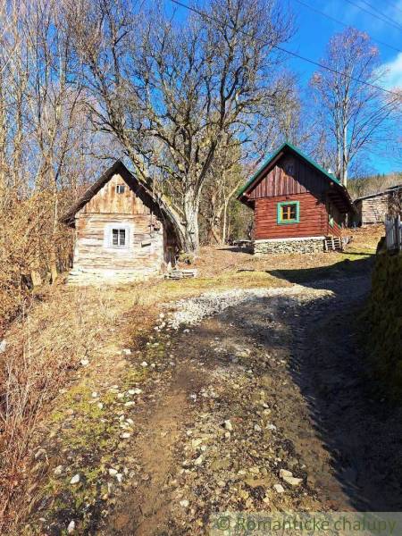 Wooden cottages amidst nature, bordered by trees and a rocky path, in a tranquil area.