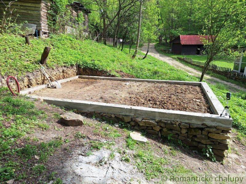 Preparing the foundation for a cabin with overgrown nature and tools next to an old house.