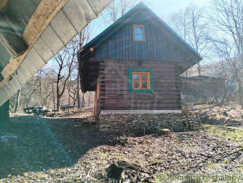 A wooden cabin surrounded by forest and a picnic table create a peaceful natural atmosphere.