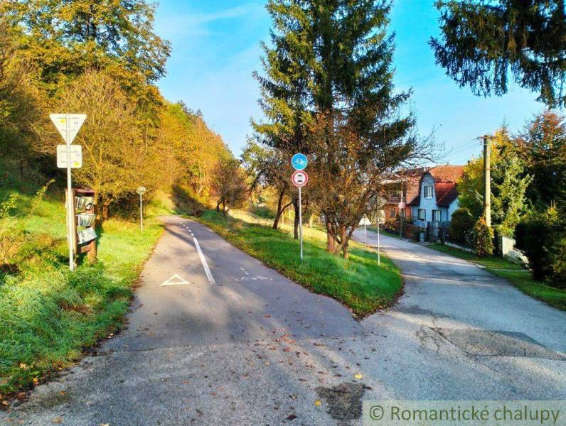 A road with traffic signs and surrounding trees leads to houses and residential plots.