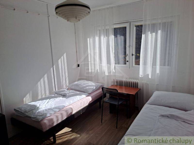 A simple room with two beds, a table, windows, and commercial spaces next door.