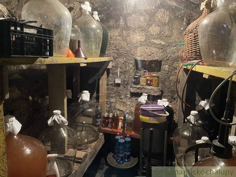 A cellar with demijohns, wine, and drinks, hidden in a stone cottage.