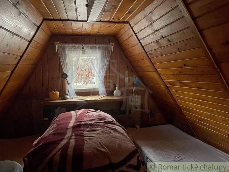 The attic of a wooden cabin with a skylight and cozy beds.