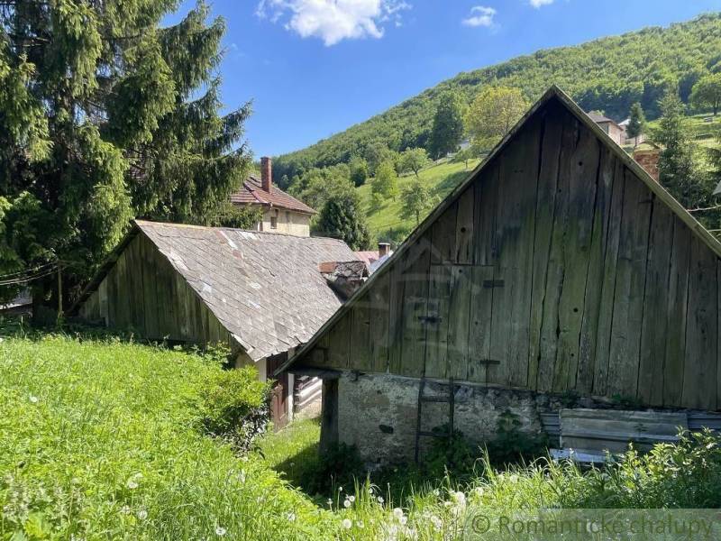 In a rural mountainous landscape, there is an ancient wooden house surrounded by nature.
