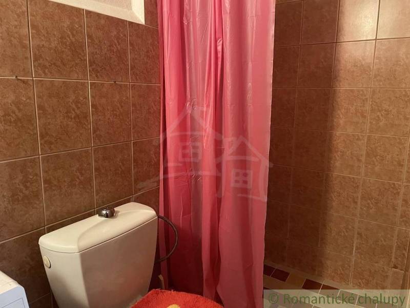 A bathroom with a pink curtain, brown tiles, and a toilet in a family house.