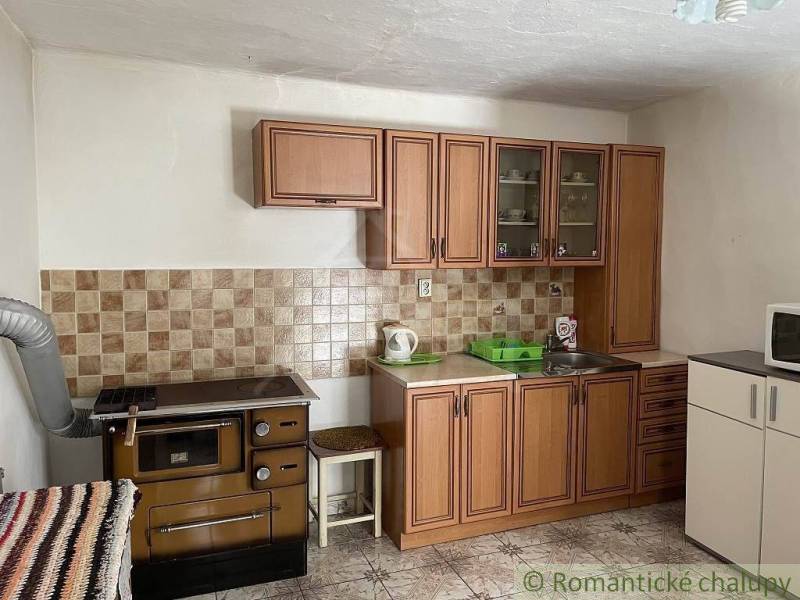 A kitchen with wooden cabinets, an old stove, dishes, and a sink in a family house.